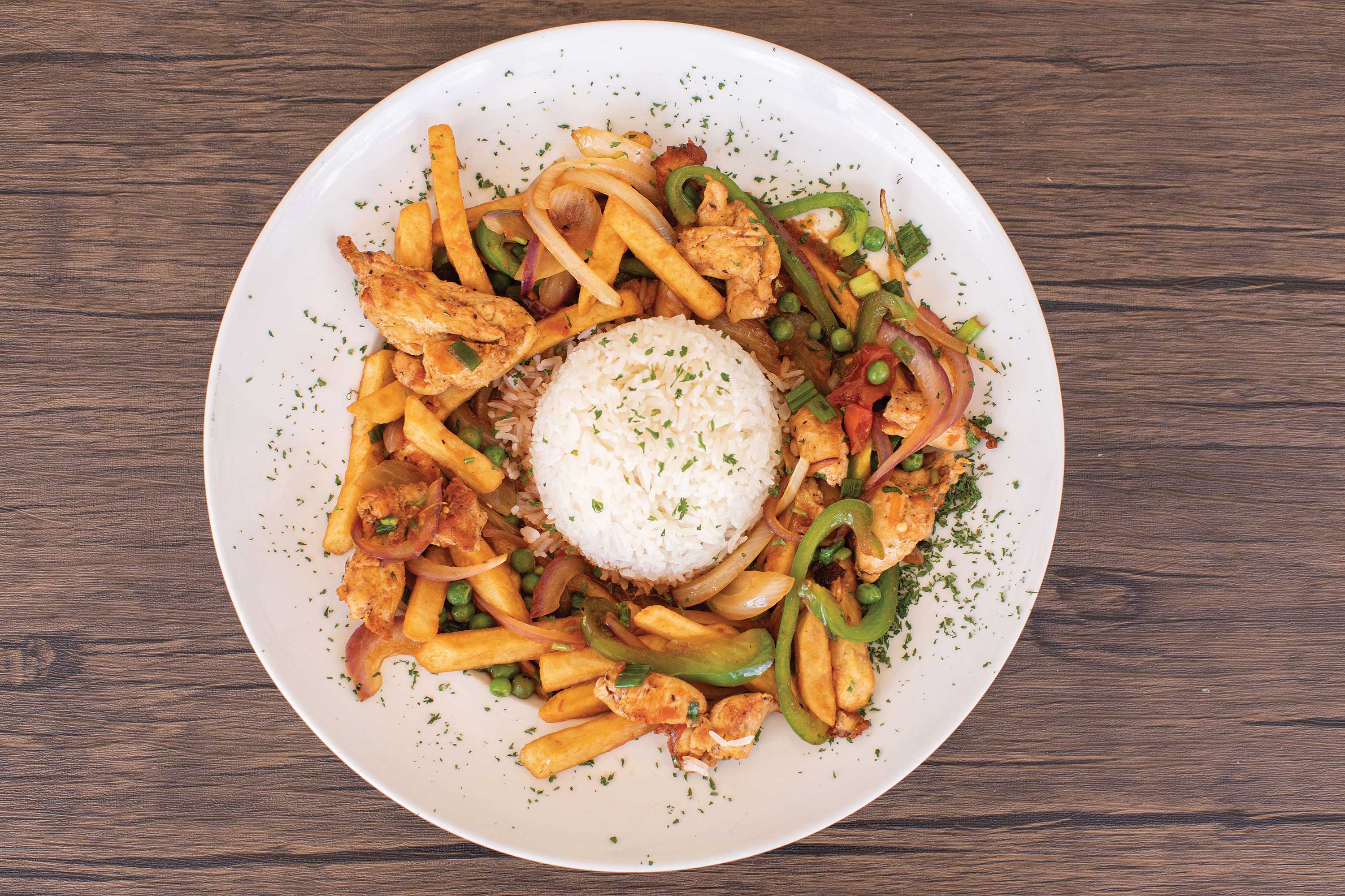 Image: Diced chicken mixed with grilled vegetables and french fries surrounded a mound of white rice. Food served in a shallow white bowl.