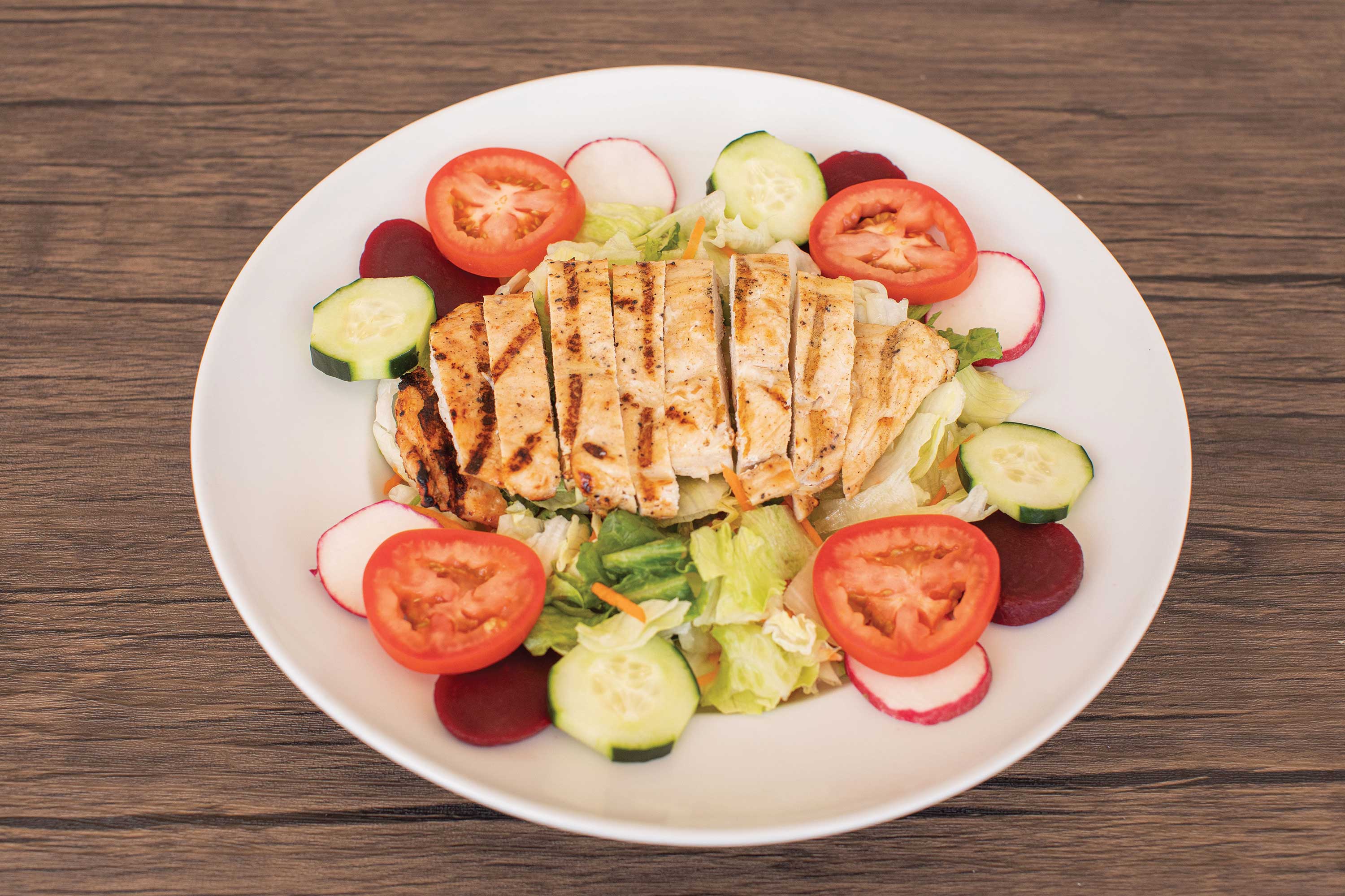 Image: A lettuce and green leaf salad is topped with a sliced chicken breast surrounded with slices of tomato, radish, cucumbers, and beets.