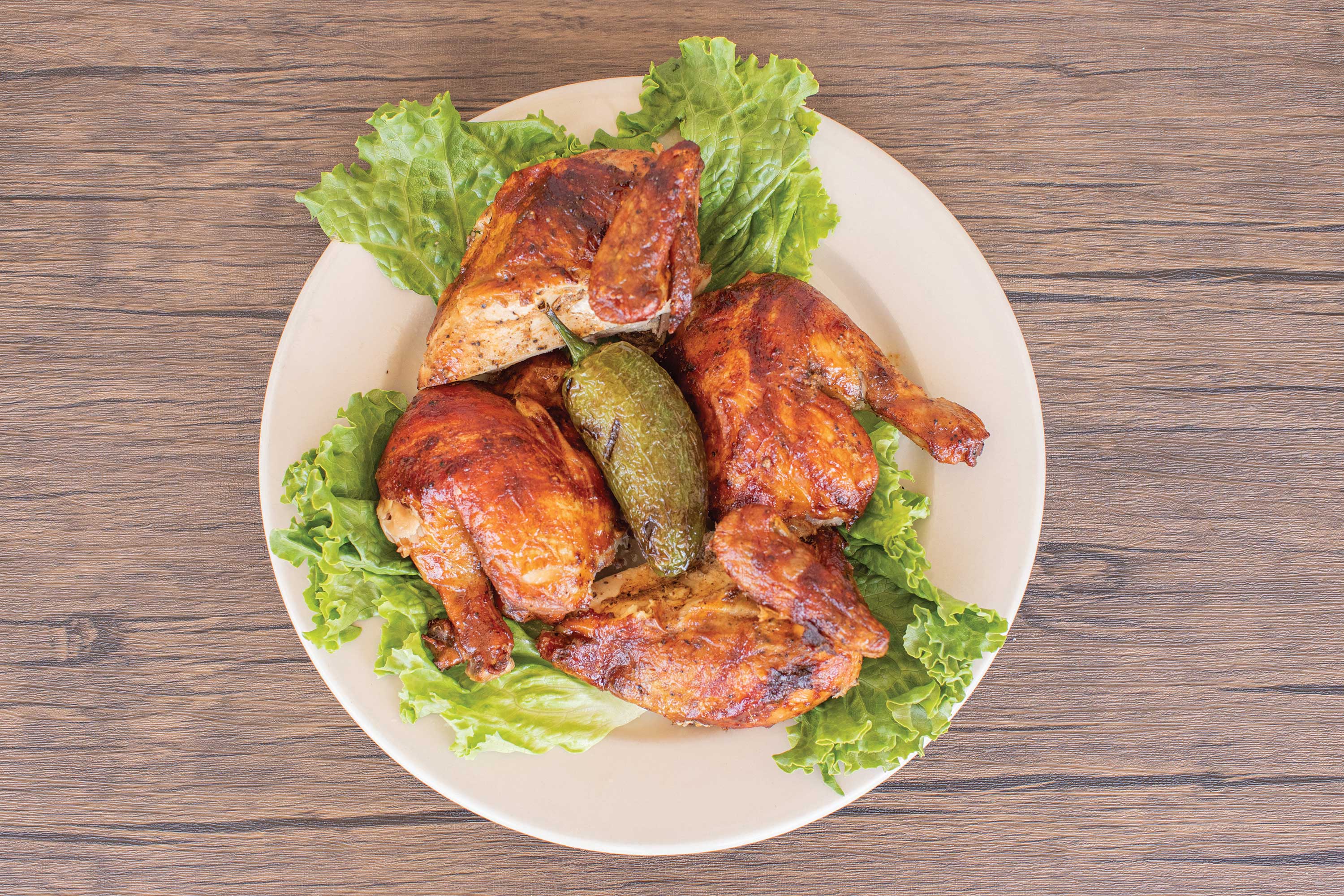 Image: Quartered Rotisserie Chicken on a bed of lettuce on top of a white plate